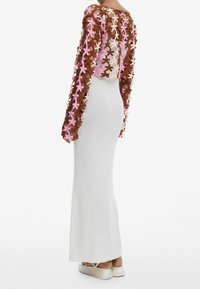 Lang, tætsiddende hvid kjole med et tekstureret brunt og pink blomstret blondeoverlag på lange ærmer. Gulvlængde med minimale accentdetaljer.