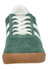 Zapatillas de ante verde con rayas blancas, cordones planos, suela de goma texturizada y punta redondeada. Interior de color claro con la marca en la lengüeta.