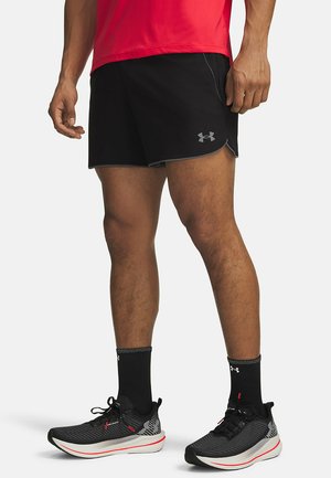 Zwarte hardloopshorts met een reflecterend logo, contrasterende grijze bies, gecombineerd met zwarte sportschoenen met rode accenten en een gestructureerd ontwerp.