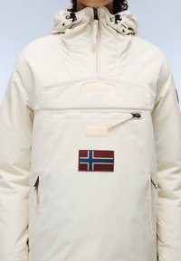 Hvit vanntett hettegenser med lomme foran, justerbar hette, glidelåsdetaljer og et ullmerke med det norske flagget.