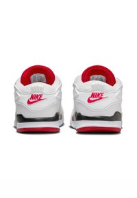 Zapatillas blancas con acentos rojos, suela negra, cuello acolchado rojo y unidad de aire visible; presenta la marca Nike en el talón y en el costado.