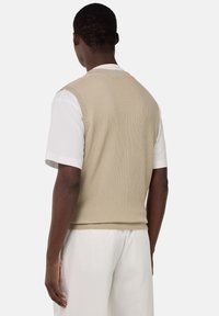 Gilet en tricot beige, texture côtelée, sans manches, porté sur une chemise blanche, vu de dos. Tissu doux, coupe décontractée.