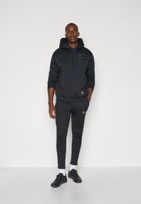 Black hoodie with front pocket and drawstring, paired with matching joggers. Both garments feature subtle logo accents and a slim fit.
