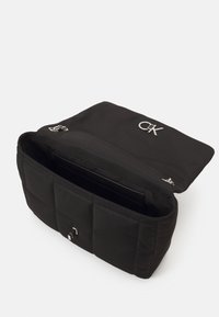 Černá prošívaná nylonová taška se stříbrným logem a hardwarovými doplňky. Disponuje otevřeným vrchem a prostorným interiérem pro uložení.