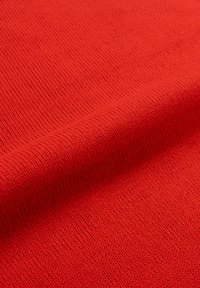 Il tessuto lavorato a maglia rosso presenta una consistenza liscia e un motivo uniforme, con cuciture visibili e una leggera caduta.