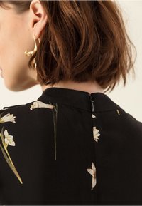 Černé květinové šaty s kulatým výstřihem, zadním zipem a jemnými bílými květinami s zelenými stonky. Hladká látka a strukturovaný střih.