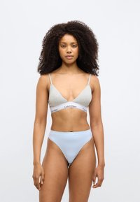 Ανοιχτό γκρι σουτιέν bralette με λεπτές τιράντες, με λωρίδα λογότυπου Calvin Klein· συνδυασμένο με σλιπ ανοιχτού μπλε χρώματος με ψηλό κόψιμο, λεία υφή.