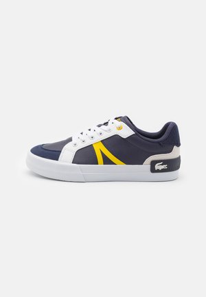 Zapatillas navy con acentos en blanco y amarillo, con un respaldo texturizado, diseño de cordones y una suela de goma en contraste. Logo de Lacoste en el lateral.