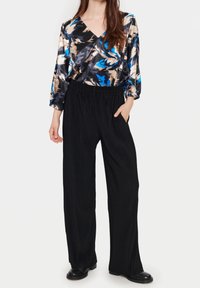 Blus i satin med blommönster i blå och beige nyanser, med V-ringning och långa ärmar, parat med svarta ribbade vida byxor.