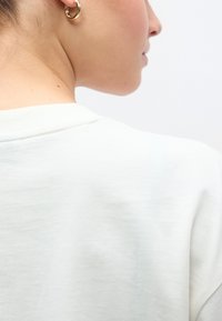 Ελαφρώς υφασμένο, εκρού βαμβακερό μπλουζάκι με μέτριο στρογγυλεμένο λαιμόκοψη, που διαθέτει εμφανές ράψιμο στο πίσω μέρος και απαλό ύφασμα που πέφτει ομαλά.