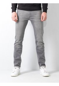 Jeans gris ajustados hechos de mezclilla, con un acabado ligeramente desvaído, costuras sutiles y dobladillos enrollados. Combinados con zapatillas blancas.