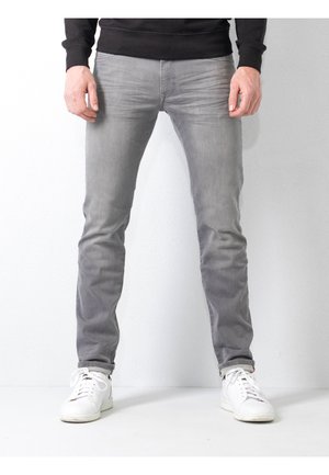 Jeans grigi stretti realizzati in denim, con una leggera finitura sbiadita, cuciture sottili e orli risvoltati. Abbinati a sneakers bianche.