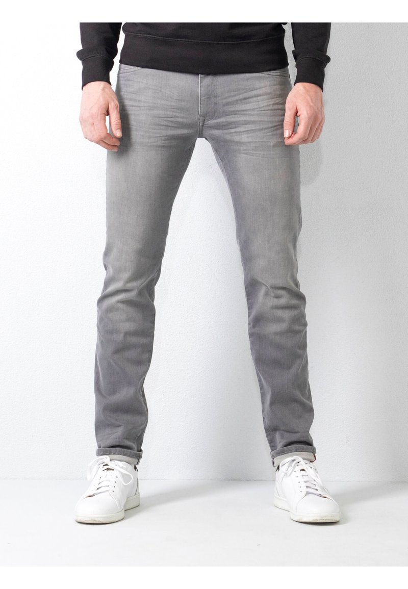 Jeans gris ajustados hechos de mezclilla, con un acabado ligeramente desvaído, costuras sutiles y dobladillos enrollados. Combinados con zapatillas blancas.
