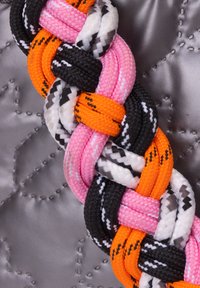 Cinghia intrecciata in nylon nei colori rosa, arancione, nero e bianco, con una superficie testurizzata su uno sfondo argento trapuntato.