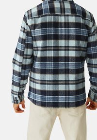 Camicia in flanella a quadri blu e navy con colletto, maniche lunghe e vestibilità rilassata. Il tessuto appare tessurizzato con accenti marroni a contrasto.