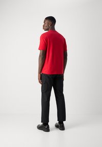 Red short-sleeve t-shirt, paired with black cargo pants. The outfit features a relaxed fit with a crew neckline and black footwear.