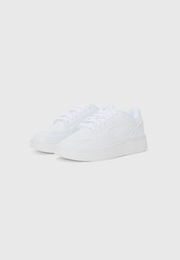 Hvite joggesko laget av glatt syntetisk materiale, med rund tå, hvite snørebånd, teksturerte såler og en logo på siden.