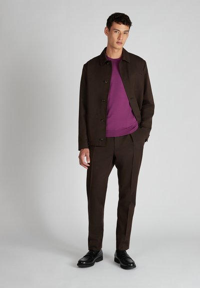 Giacca marrone, camicia viola e pantaloni marroni. La giacca ha bottoni e tasche; le scarpe sono nere e lucidate.