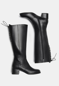 Bottes en cuir noires montantes jusqu'aux genoux avec de petits talons blocs, zips latéraux et détails en lacets à l'arrière, présentées de profil et par le dessous.