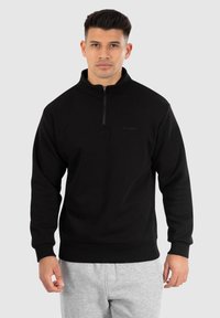 Zwarte zip-up sweatshirts gemaakt van zacht materiaal, met een hoge kraag, geribde manchetten en een klein logo op de borst.