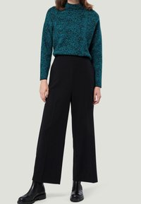 Pull marin à col roulé bleu sarcelle à motifs, associé à un pantalon noir à taille haute et jambes larges. Chaussures : bottines noires à semelles épaisses.