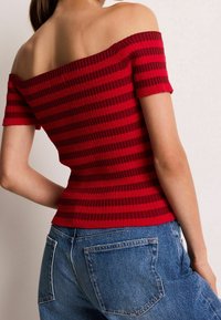 Red off-the-shoulder top with horizontal stripes, ribbed texture, short sleeves, paired with blue high-waisted jeans featuring back pockets.