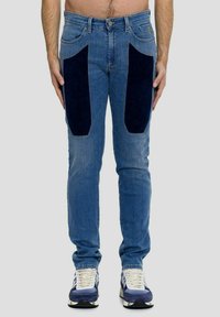 Jeans blu con pannelli in corduroy blu scuro sulle cosce, vestibilità slim, cinque tasche e classica texture in denim. Abbinati a sneaker bianche e blu.