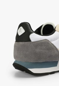 Sneaker mit einem grauen Wildleder- und schwarzen Mesh-Obermaterial, weißen Akzenten, strukturierten Gummisohlen und einem Totenkopf-Logo auf der Ferse.