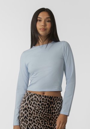 Crop top bleu clair à manches longues en tissu lisse, associé à une jupe léopard taille haute avec de grandes taches noires.