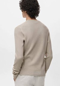 Maglione beige a coste con maniche lunghe e collo rotondo. Presenta una finitura testurizzata e una silhouette aderente. Dietro è semplice, senza decorazioni.