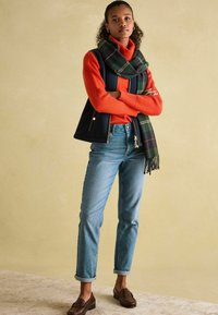 Červený pletený sveter, námornícky vest, zelený károvaný šál, svetlomodré džíny s vysokým pásom, rozrolované manžety, hnedé mokasíny, na neutrálnom pozadí.