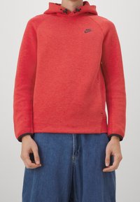Röd huvtröja i texturerad väv, med dragsko i huvan och svarta detaljer. Har en liten svart Nike-logga på bröstet och en avslappnad passform.