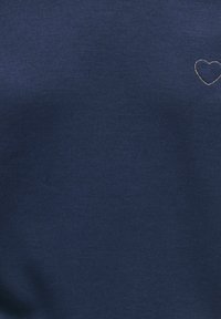 Tissu bleu foncé avec un petit cœur cousu de couleur claire dans le coin supérieur droit.