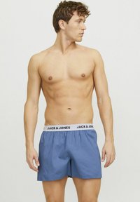Shorts de bain bleus avec une ceinture élastique portant "JACK & JONES" en noir. Tissu léger, coupe ample et texture lisse.