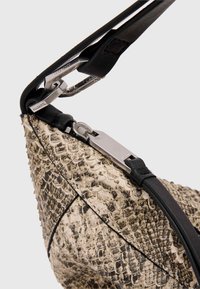 Musta nahkavöö ühendub tekstureeritud beeži ja pruuni rästikukujulise mustriga kotiga. Omab hõbedast riistvara ja tõmbeklappi.