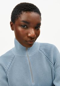 Lichtblauwe trui met ritssluiting, hoge kraag, geribbelde structuur en een zilverkleurige ritsaccent, met raglanmouwen en een getailleerd ontwerp.