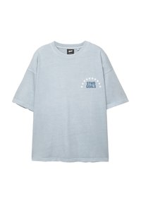 Lyseblå kortærmet T-shirt med rund hals, der har teksten "STWD GOALS" under en halvcirkel af hvide stjerner på venstre bryst.