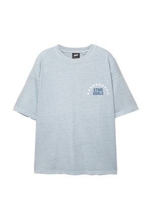 Vaaleansininen lyhythihainen T-paita, jossa on pyöreä pääntie. T-paidassa on "STWD GOALS" -teksti, joka sijaitsee vasemmassa rinnassa valkoisten tähtien puoliympyrän alla.