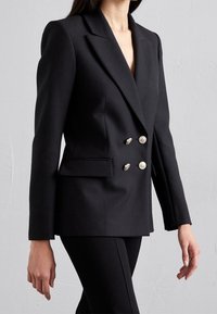 Blazer nero doppiopetto realizzato in tessuto sartoriale, caratterizzato da revers a punta, due tasche frontali e bottoni decorativi silver.