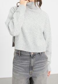 Ljusgrå mössa med ribbat halsringning och ärmslut, kombinerad med urtvättade grå högmidjade jeans med subtila sömmar och knappdetalj.