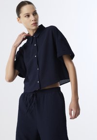 Marineblauwe cropped shirt van een textuurstof, met korte mouwen en een knoopsluiting aan de voorkant, gecombineerd met bijpassende elastische broek met een tailleband.