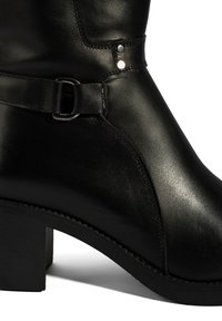 Zwarte leren enkelboot met een ronde neus, voorzien van een decoratieve band en gespdetails, en een lage, stevige hak. Soepele textuur.