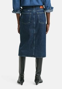 Denim A-lijnrok in donkerblauw met een split aan de achterkant. Voorzien van twee achterzakken en een leren label op de tailleband. Gekocht met kniehoge laarzen.