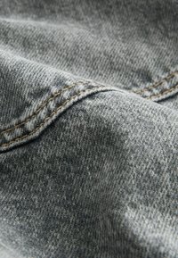 Hallhallane denimpind, millel on tekstureeritud pind, nähtavad õmblused kontrastse värviga ääres, luues peene mustri.