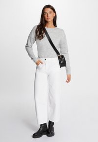 Maglione grigio lavorato a maglia, jeans bianchi a vita alta e a gamba larga con dettagli di perline, e stivali neri alla caviglia. Borsa a tracolla nera.