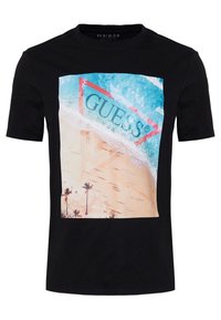 Camiseta negra con un estampado colorido de escena de playa, con un prominente logo triangular rojo y palmeras en la parte inferior.
