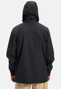 Čierna kapucňová bunda s voľným strihom, vyrobená z ľahkého materiálu. Má vysoký golier, minimálne švy a žiadne viditeľné kovania alebo vrecká.