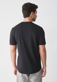 Black short-sleeve t-shirt with a round neckline, smooth texture, and relaxed fit, paired with light gray textured trousers.