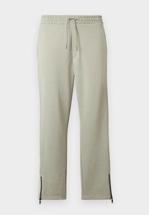 Ανοιχτόγριμες φόρμες με ελαστική μέση, κορδόνι και μαύρες λεπτομέρειες με φερμουάρ στα τελειώματα των αστραγάλων, τοποθετημένες επίπεδα σε λευκό φόντο.