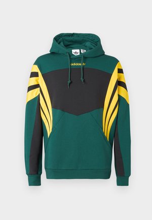 Zaļš džemperis ar melnu krūtīm, dzeltenām un melnām svītrainām piedurkņu detaļām, priekšējo kabatu un Adidas logo zem kapuces.